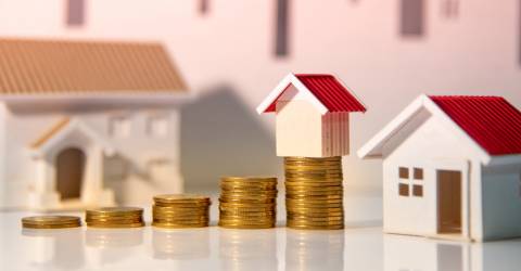 stapeltjes geld die steeds hoger worden met op de achtergrond huizen